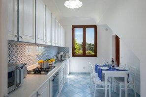 A compact kitchen with white cabinets, a tiled backsplash, and a dining area with a table set for four. - Casa Olga, with a view of the sea (Praiano)