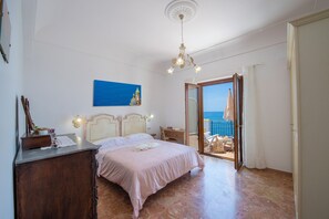 A bedroom with a bed, a desk, a chair, a painting, and a view of the sea through an open door. - Casa Olga, with a view of the sea (Praiano)