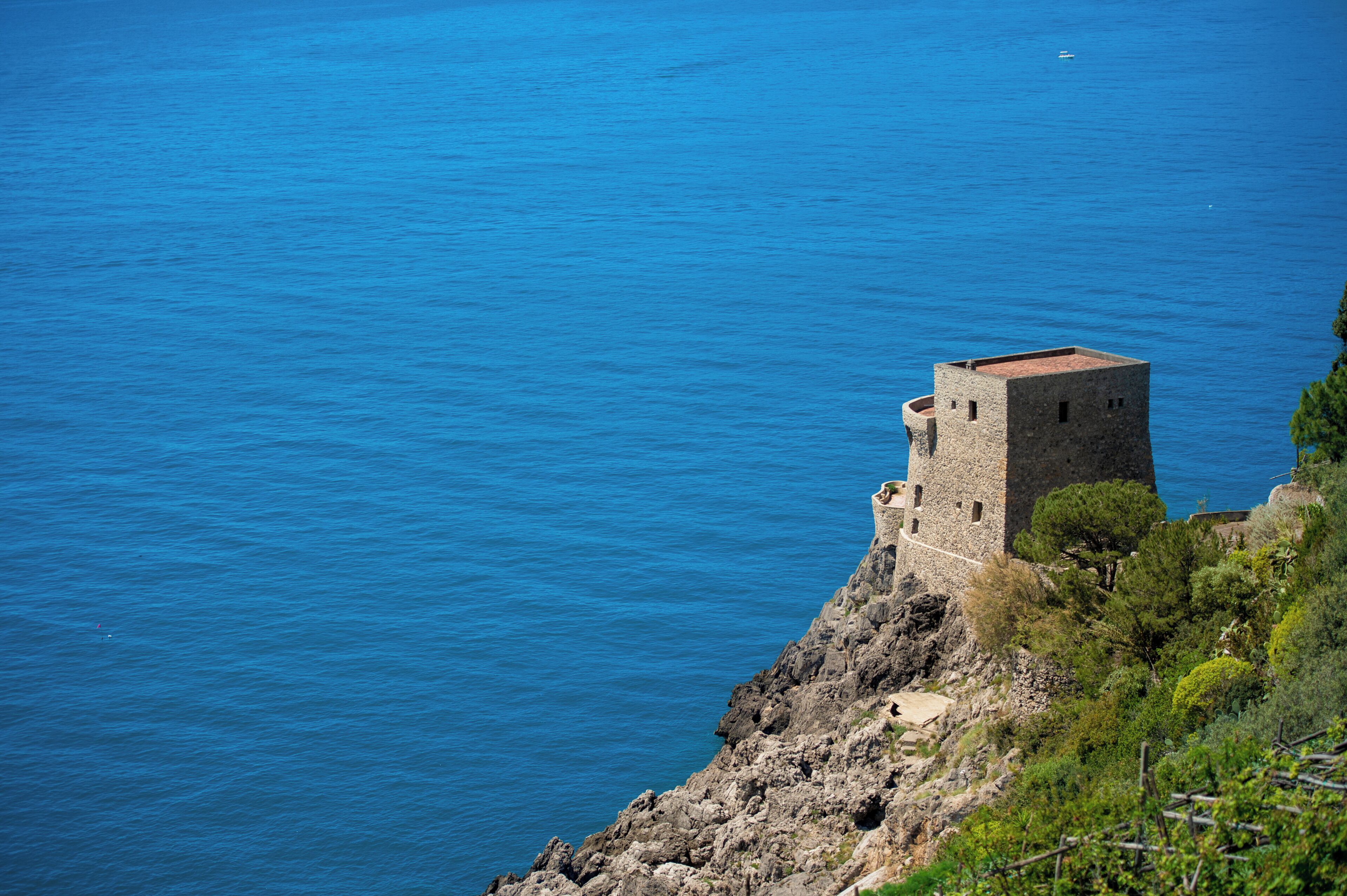 A coastal stone tower with a flat roof, overlooking a clear blue sea.