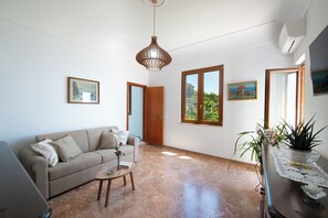 A living room with a sofa, a coffee table, a pendant light, and a view through a window. - Casa Olga, with a view of the sea (Praiano)