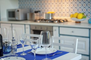 A dining table set with wine glasses, plates, and cutlery, with a kitchen in the background. - Casa Olga, with a view of the sea (Praiano)