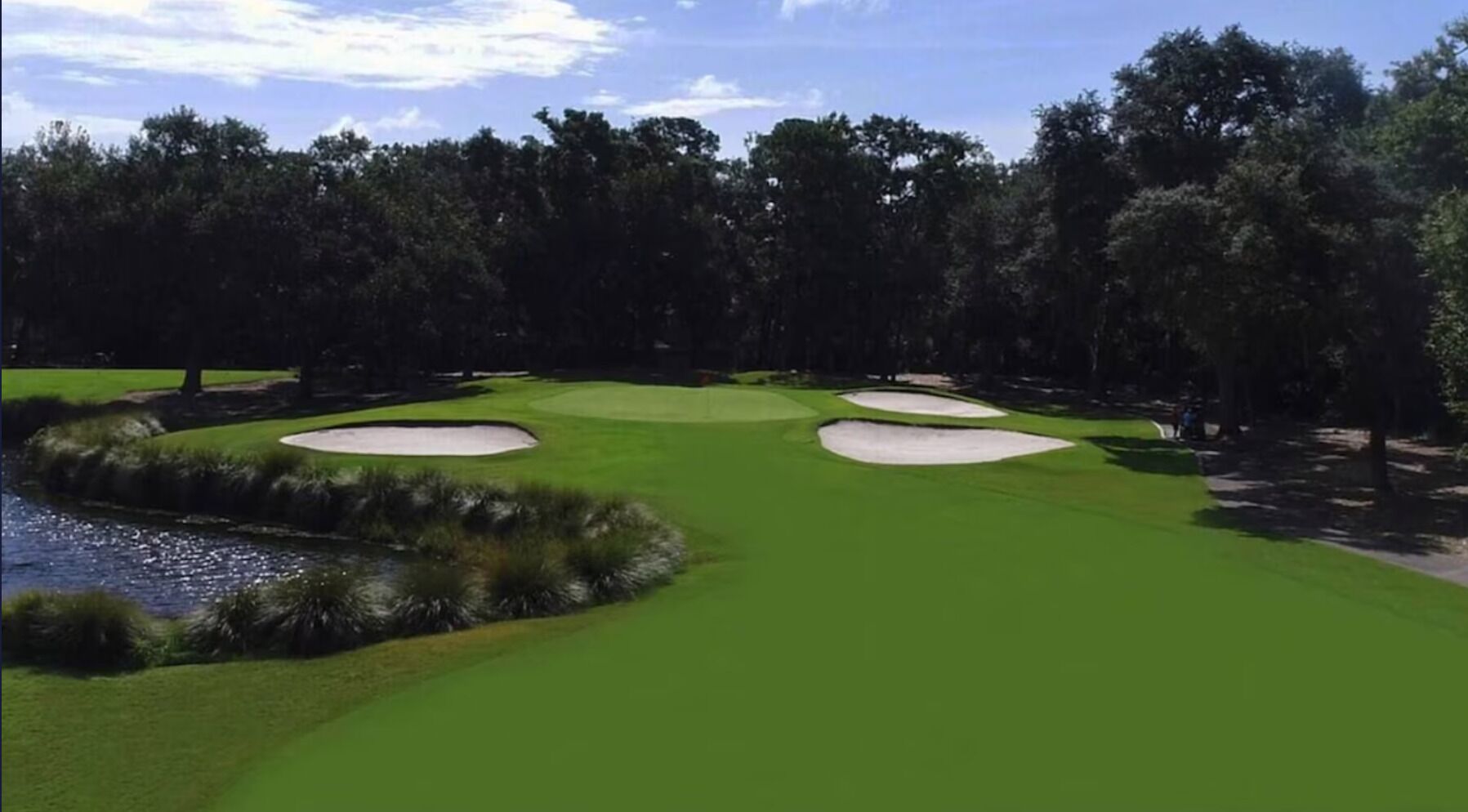 Un campo da golf con bunker di sabbia, ostacoli d'acqua e una zona boschiva.