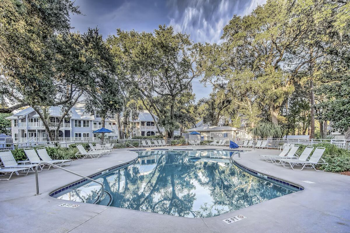 A swimming pool surrounded by lounge chairs and trees, with a view of buildings in the background.