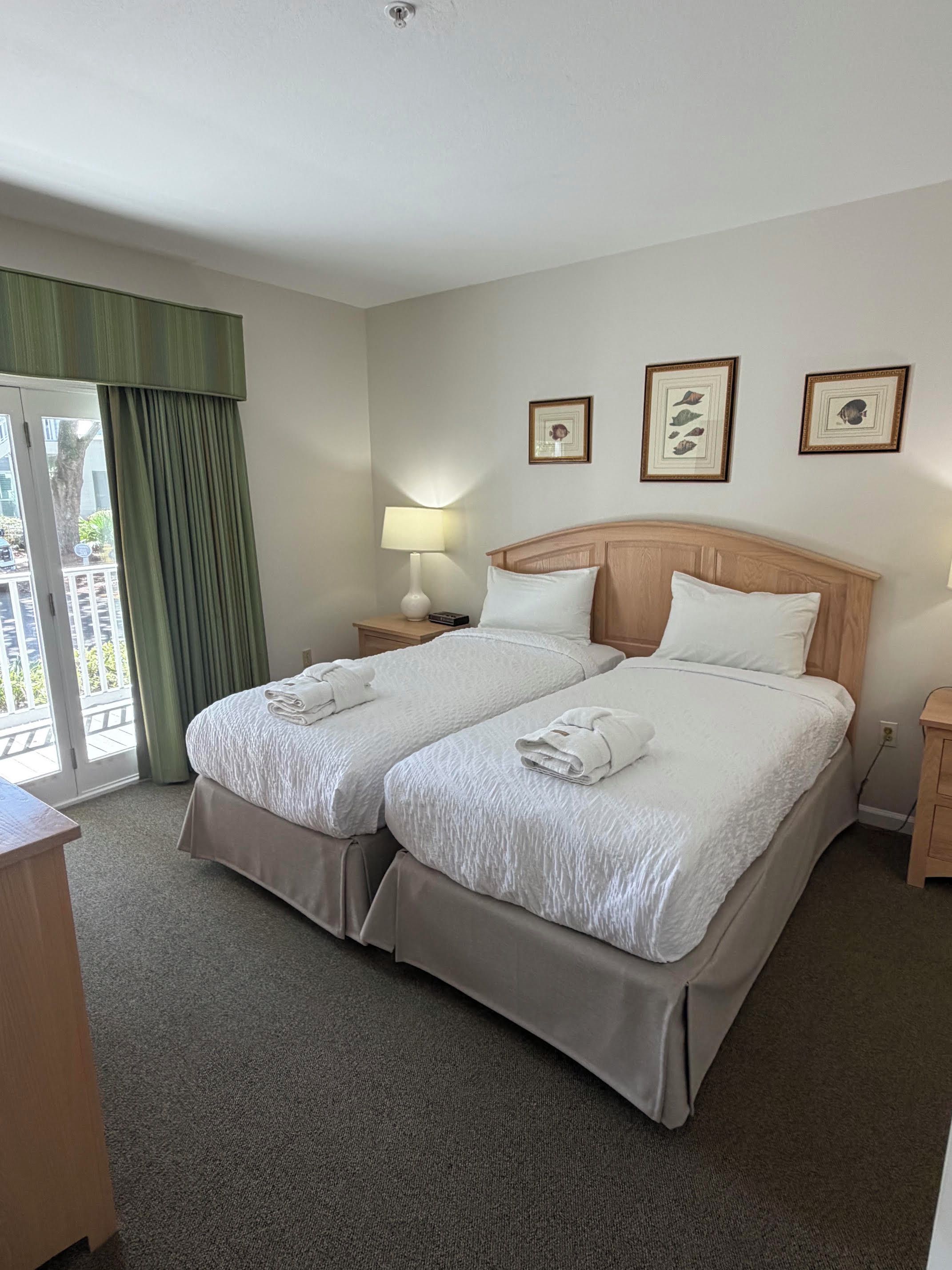 A hotel room with a double bed, two bedside tables, a lamp, and a view of the outdoors through a sliding door.