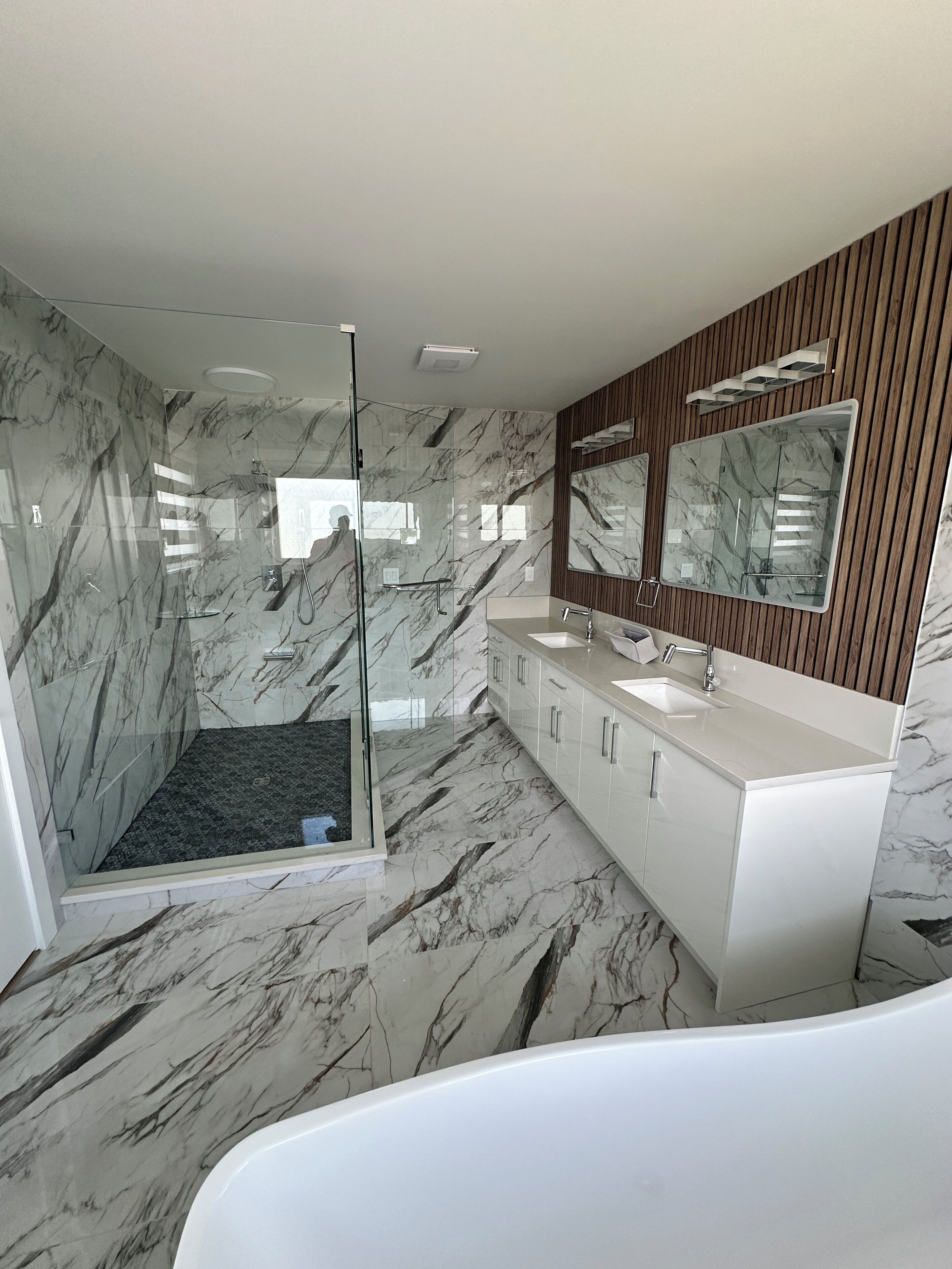 Une salle de bain moderne avec une douche à parois de verre, un grand miroir et un meuble-lavabo blanc.