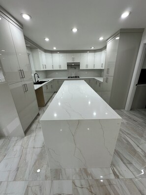 A modern kitchen with a large marble island, white cabinetry, and built-in appliances. - 5 bedroom house sleeps 12 people (Surrey)