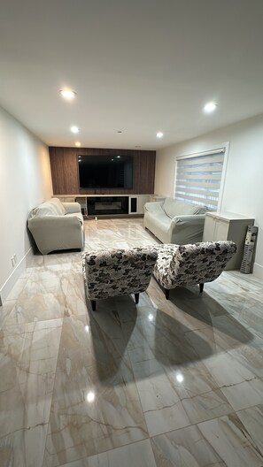 A modern living room with a flat-screen TV, two sofas, and a patterned ottoman set. - 5 bedroom house sleeps 12 people (Surrey)