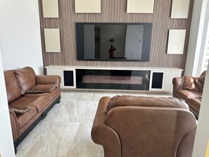 Sala de estar con una televisión de pantalla plana montada en una pared con diseño a rayas, dos sofás de cuero marrón y una chimenea debajo de la televisión.