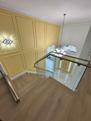 A staircase with glass railings leading to a landing with a chandelier. - 5 bedroom house sleeps 12 people (Surrey)