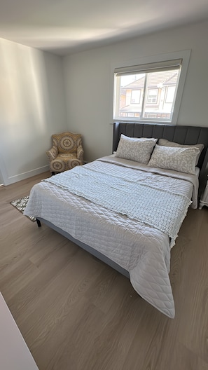 A bedroom with a large bed, a window, a patterned armchair, and a wooden floor. - 5 bedroom house sleeps 12 people (Surrey)
