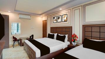 A hotel room with two beds, a desk, a chair, an air conditioning unit, and a window.