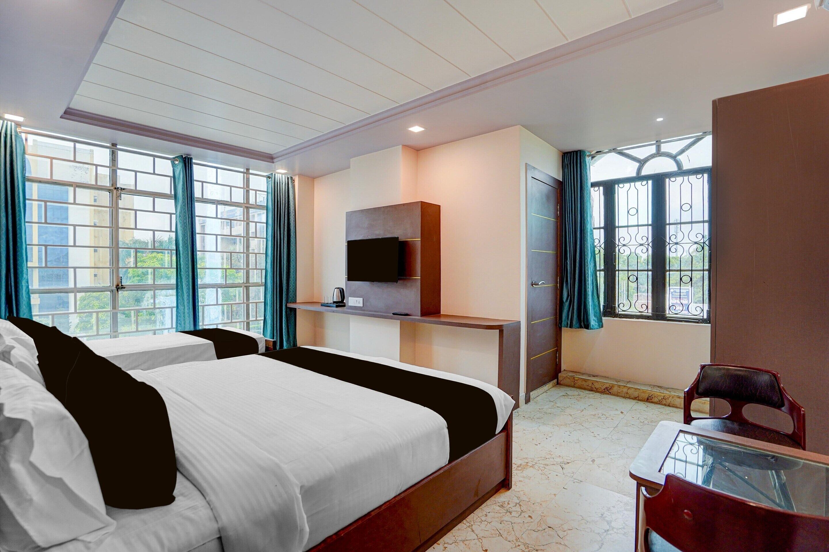 A hotel room with a bed, a desk, a TV, and a window with curtains.