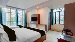 A hotel room with a bed, a desk, a TV, and a window with curtains. - Premium Family Suite With Balcony Mauji's (Prayagraj)