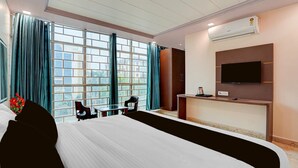 A hotel room with a large bed, a desk with a chair, a TV mounted on the wall, and an air conditioning unit. - Premium Family Suite With Balcony Mauji's (Prayagraj)