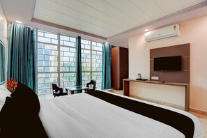 A hotel room with a large bed, a desk with a chair, a TV mounted on the wall, and an air conditioning unit.