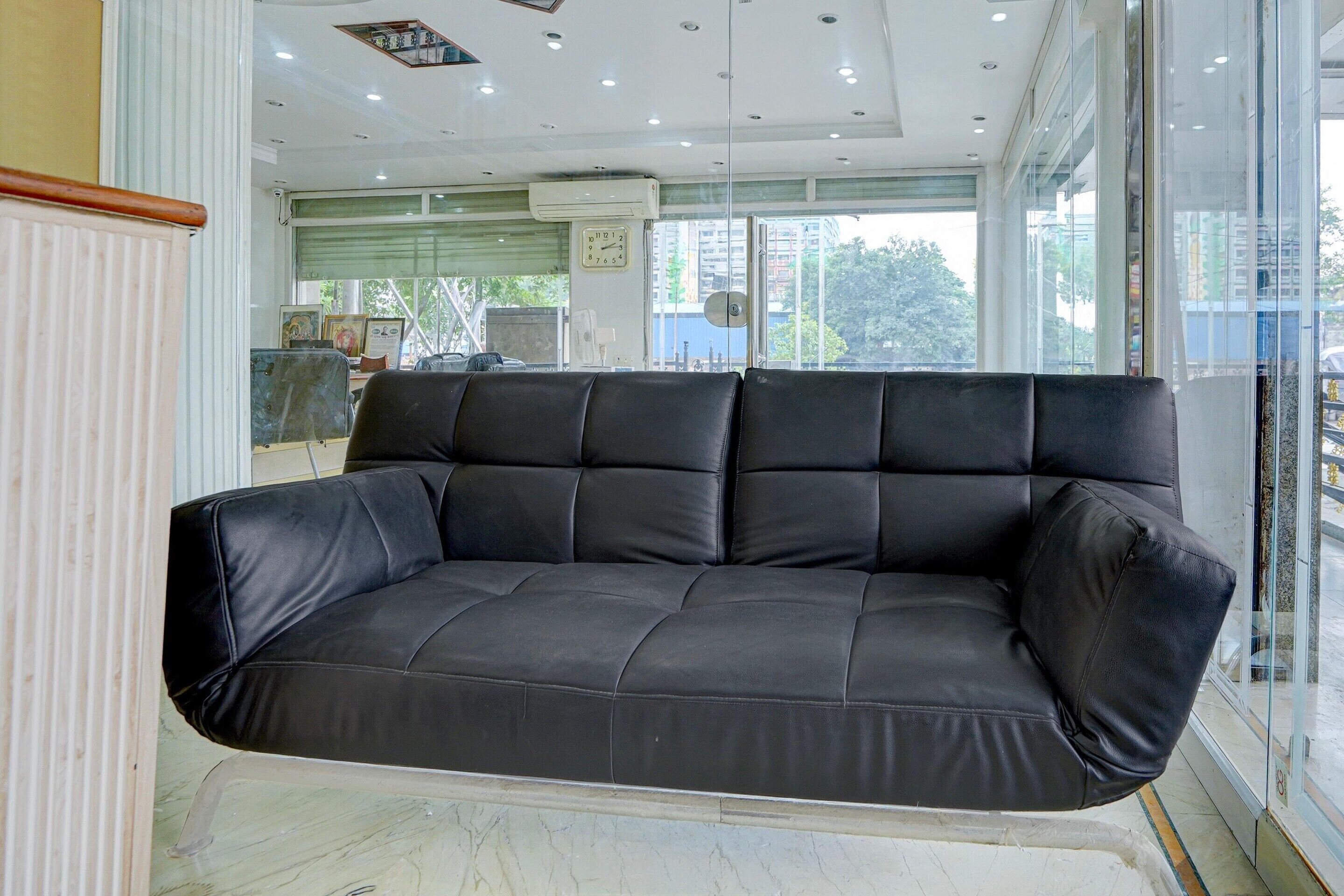 A black leather sofa in a modern room with a large window, a clock on the wall, and a ceiling with recessed lighting.