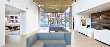 A modern hotel lobby with a reception desk, seating area, and large windows offering a view of the outdoor area.