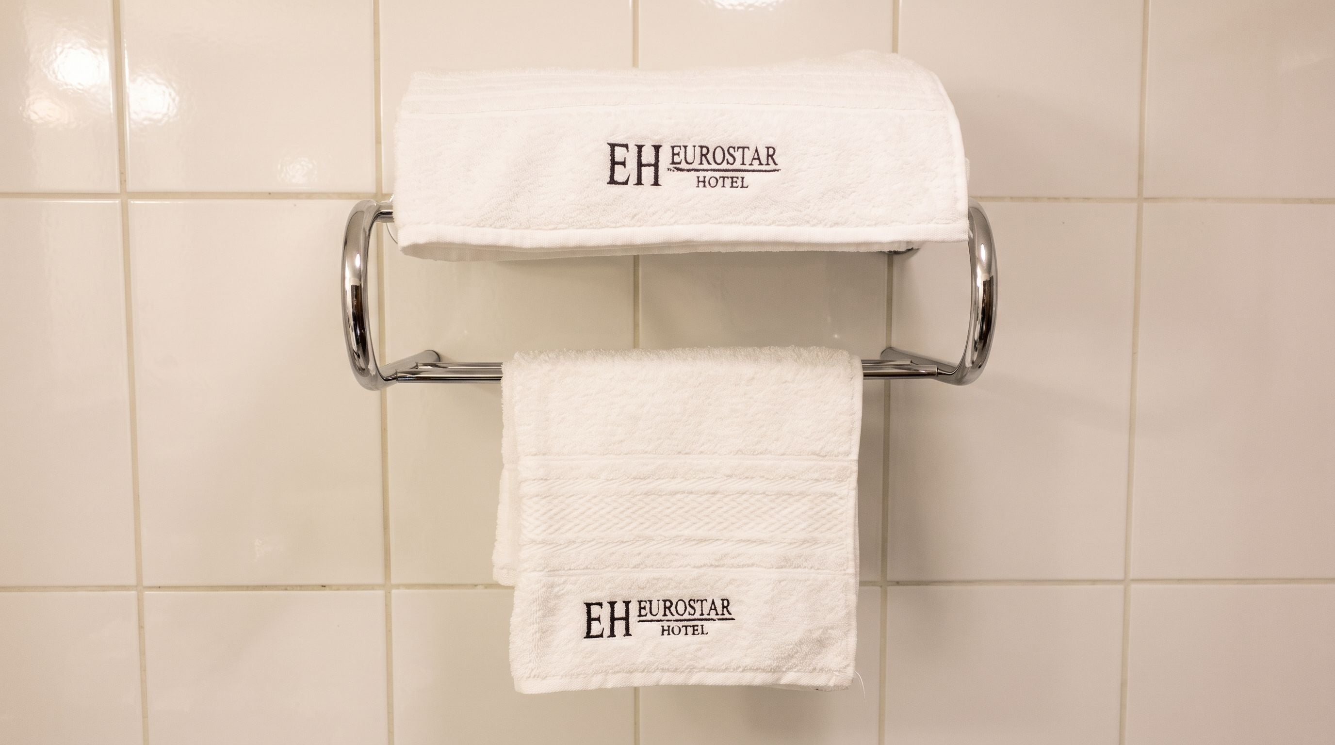 Un baño con dos toallas blancas colgadas en un toallero de cromo, ambas con la leyenda 'EH EUROSTAR HOTEL'.