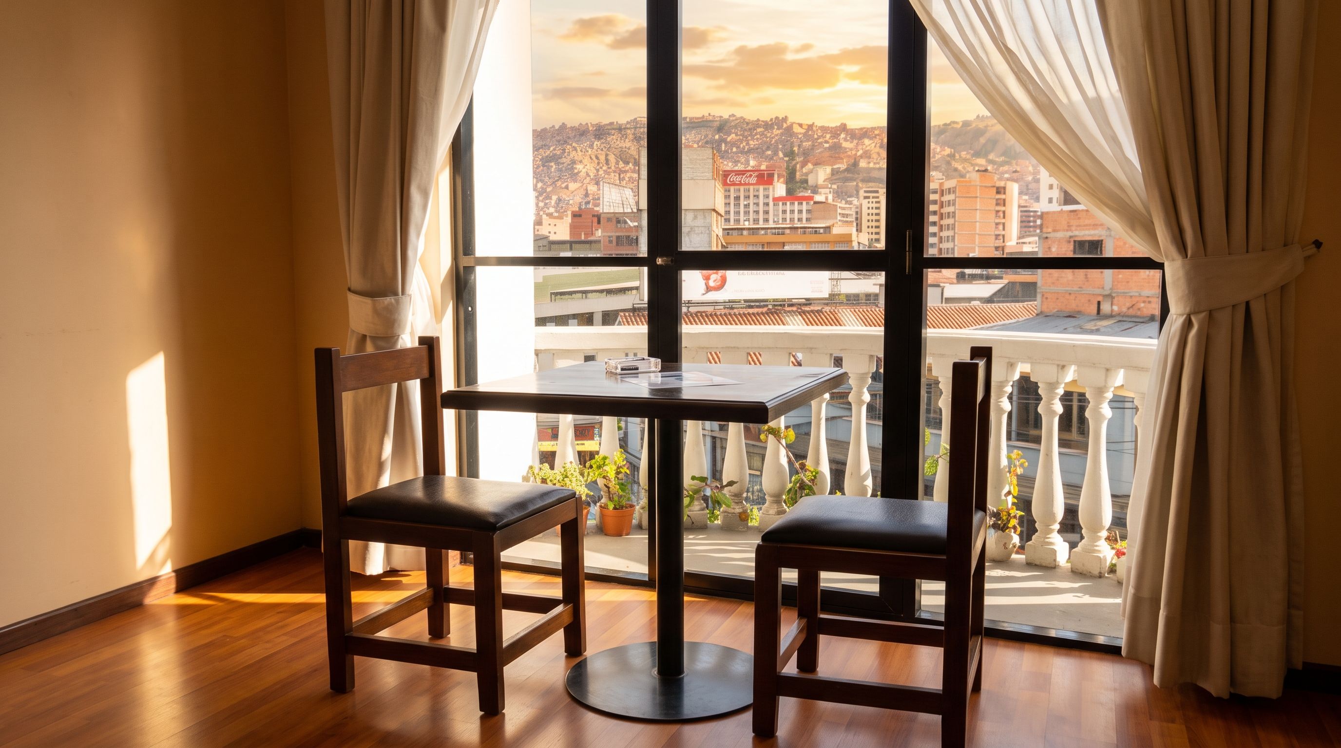 A room with a table and two chairs, a window with curtains, and a view of a cityscape.