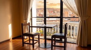 A room with a table and two chairs, a window with curtains, and a view of a cityscape. - Hotel Monte Carlo (La Paz)