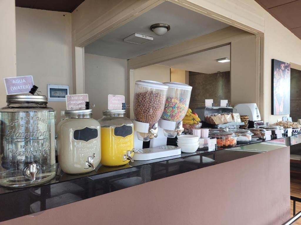 Una barra de desayuno con dispensadores para agua, jugo y leche, y recipientes para cereales y otros productos de desayuno.