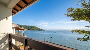 A balcony with a view of a calm sea and boats, a wooden pergola, and a clear sky. - Beautiful Beachfront House Santo Antonio Cda1647 (Florianópolis)