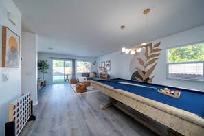 Une table de billard dans une pièce dotée d’une grande fenêtre, d’une plante et d’un mur orné d’un motif de feuilles.