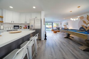 Een moderne keuken met witte kastjes, een roestvrijstalen koelkast en een bar met een pooltafel.