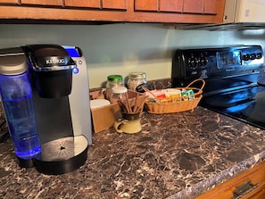 A kitchen counter with a Keurig coffee maker, a water bottle, spice jars, a mug, and a basket of items.