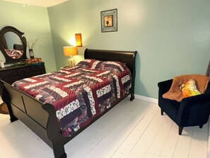 A bedroom with a bed, a chair, a dresser, a mirror, and a wall decoration.