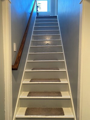 A staircase with a wooden handrail, carpeted steps, and a view of a window at the top.
