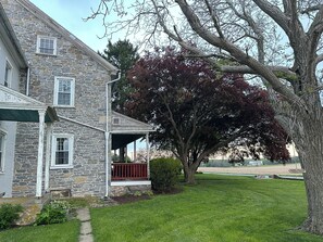 A stone house with a covered porch and a large tree with red leaves.