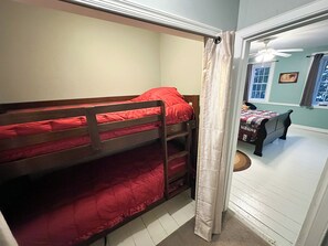 A bunk bed room with a window and a door leading to another room.