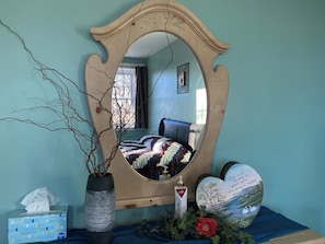A bedroom with a bed, a mirror, a vase with branches, a tissue box, and decorative items.
