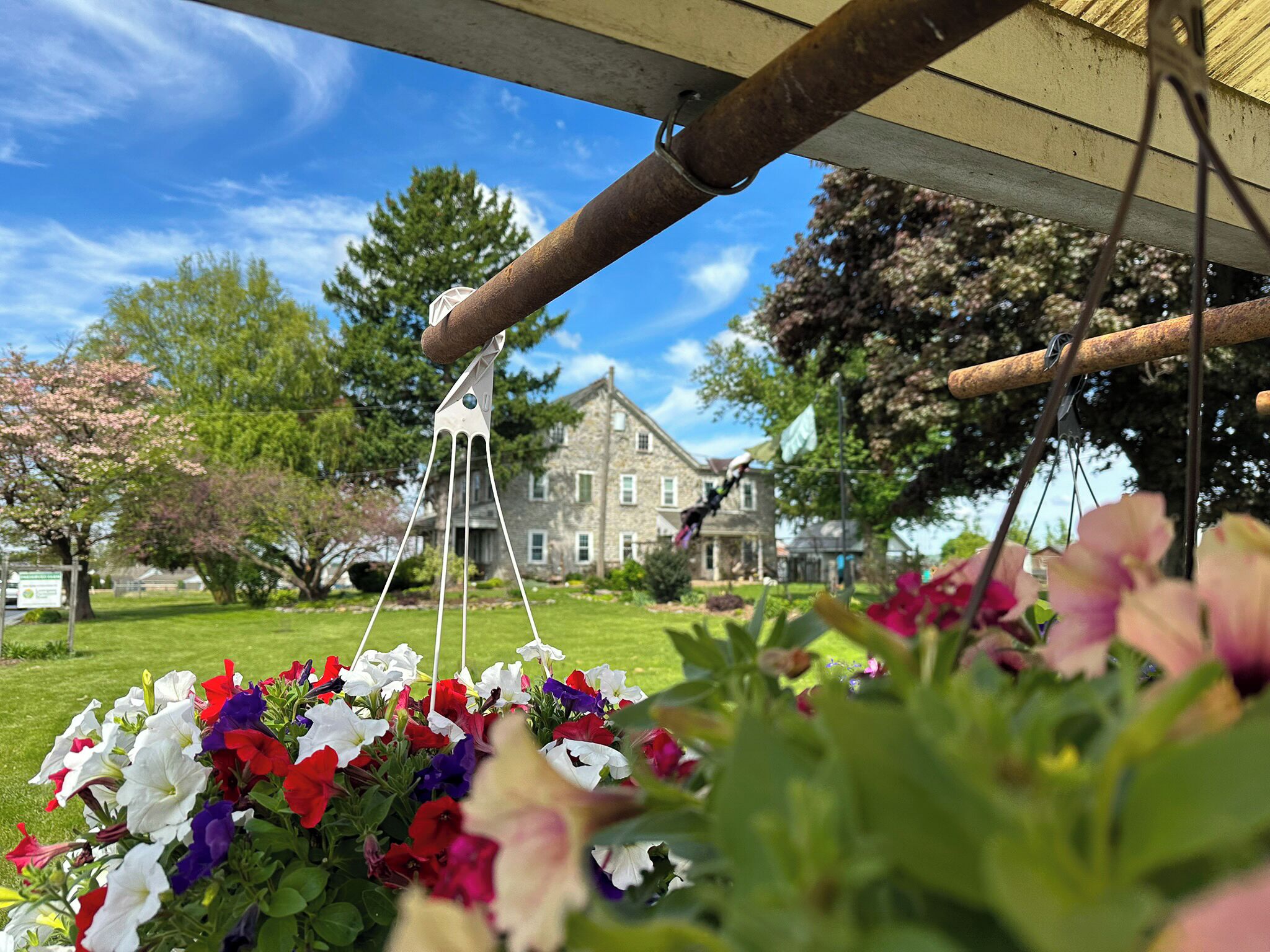 A garden with a hanging flower arrangement and a stone building in the background.