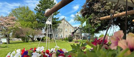 A garden with a hanging flower arrangement and a stone building in the background.