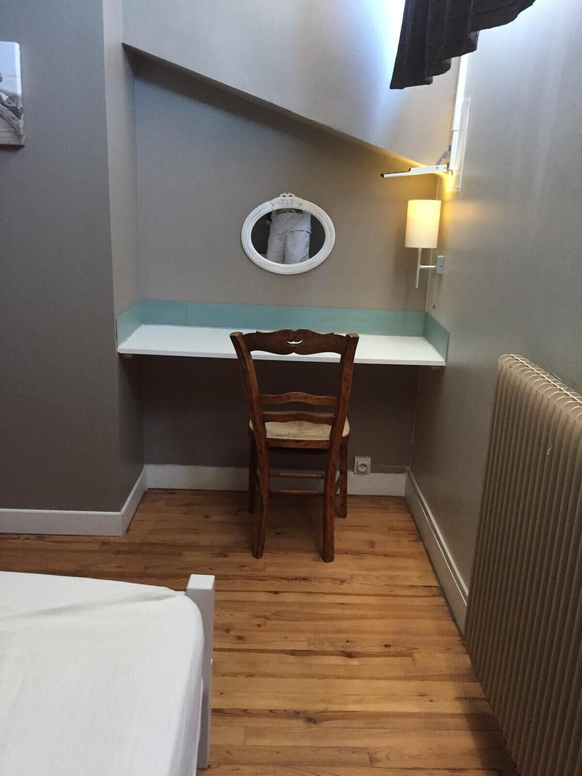A small room with a wooden chair, a white desk, a round mirror, and a wall-mounted lamp.
