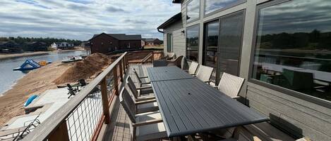 A deck with outdoor furniture, a view of the water, and a building with large windows.