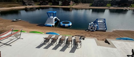 A lakeside patio with lounge chairs, a floating dock, and a small boat.