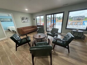 Ein großzügiger Wohnbereich mit braunem Sofa, Ledersesseln, einem Couchtisch und großen Fenstern mit Blick auf einen Pool und Gebäude.