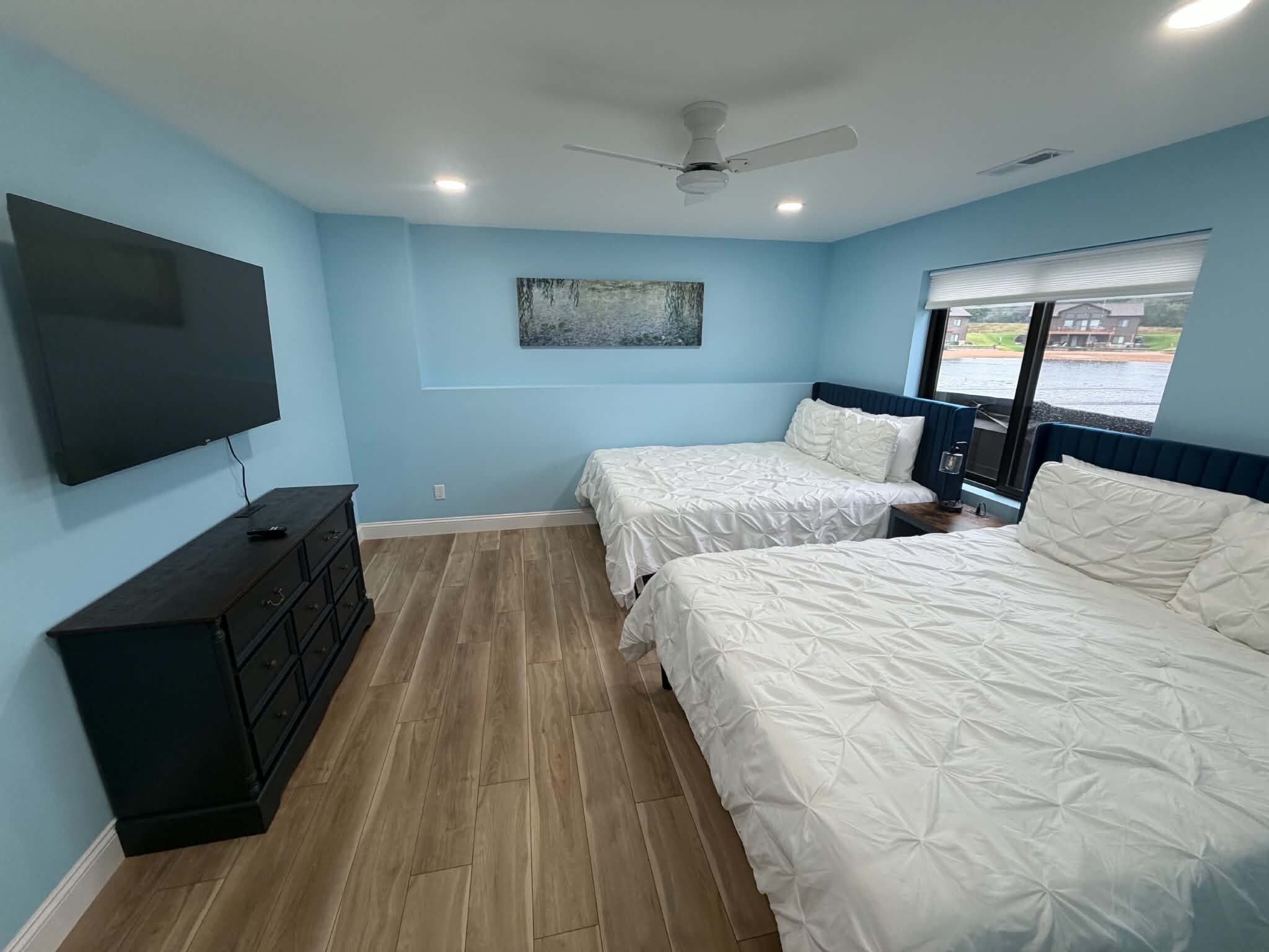 A bedroom with two beds, a TV, a ceiling fan, and a window with a view.