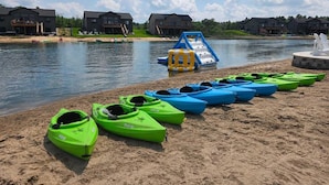 Ein Seeblick mit am Strand aufgereihten Kajaks, einer Wasserrutsche und Häusern im Hintergrund.