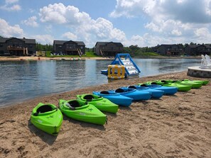 Ein Seeblick mit am Strand aufgereihten Kajaks, einer Wasserrutsche und Häusern im Hintergrund.