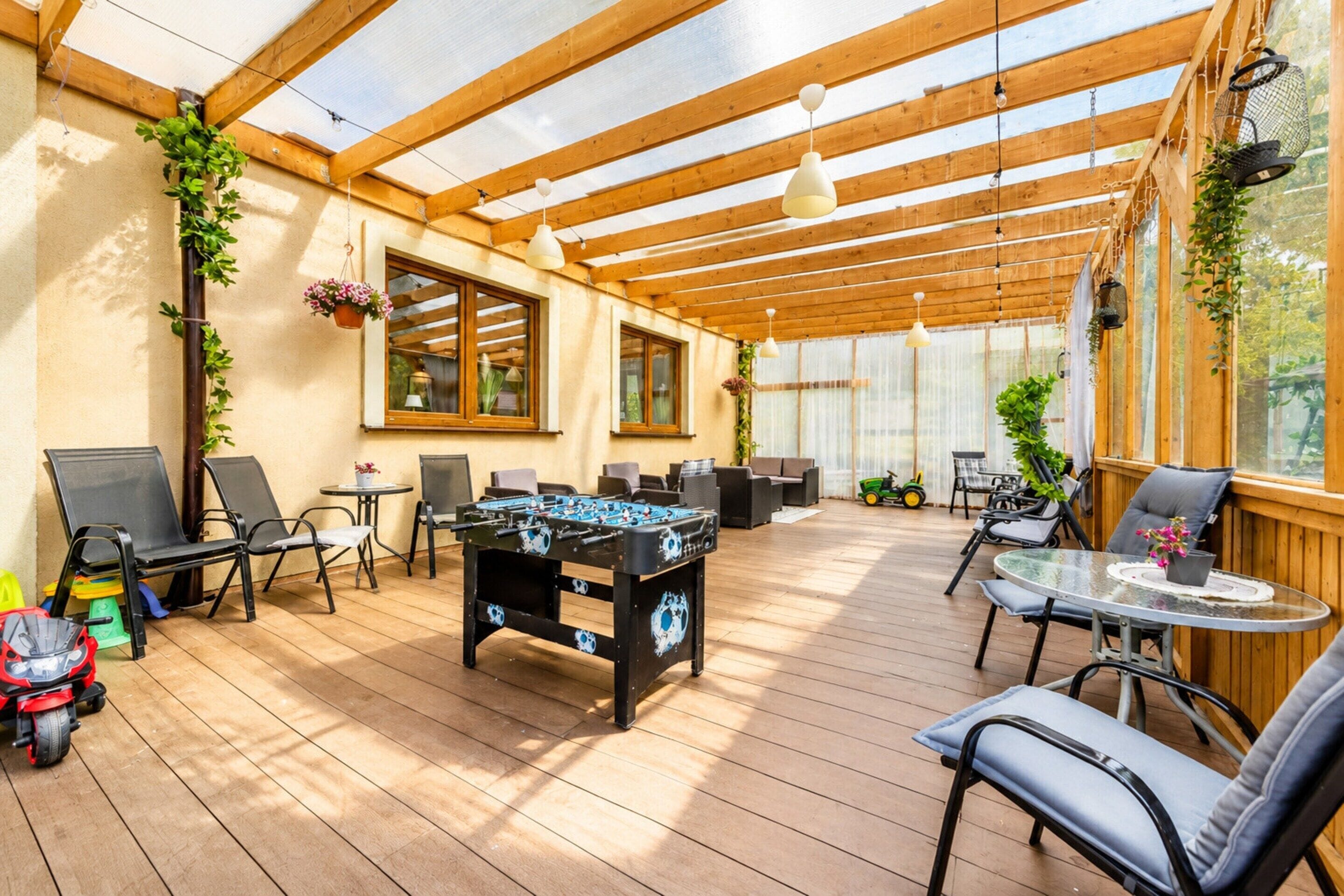 An outdoor patio area with wooden flooring, seating arrangements, a foosball table, and potted plants.