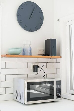 A kitchen with a microwave oven, a clock, and a shelf with a bowl and a vase. - Bayview Cottage Serene Escape between Beach and Bay (Blairgowrie)