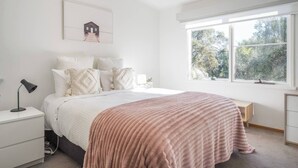 Ein Schlafzimmer mit Bett, Nachttischen, einer Lampe, einem Fenster mit Aussicht und einem Bild an der Wand.