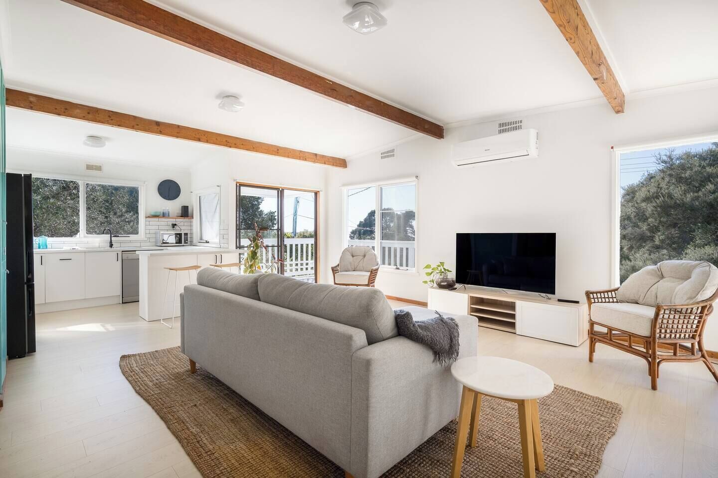 A modern living room with a sofa, TV, and seating area, connected to a kitchen with a balcony.