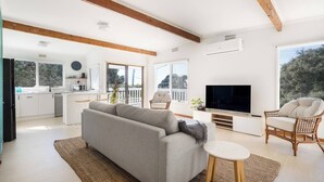 Ein modernes Wohnzimmer mit Sofa, Fernseher und Sitzecke, verbunden mit einer Küche und einem Balkon.