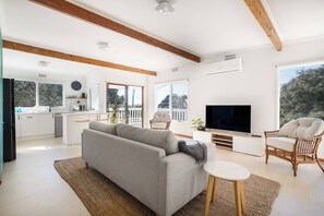 A modern living room with a sofa, TV, and seating area, connected to a kitchen with a balcony. - Bayview Cottage Serene Escape between Beach and Bay (Blairgowrie)