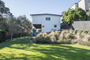 A single-story house with a covered porch, surrounded by a well-maintained lawn and a wooden fence. - Bayview Cottage Serene Escape between Beach and Bay (Blairgowrie)